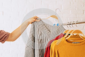 Woman& x27;s hand removes grey knitted jacket on wooden hanger from an iron rack rale photo