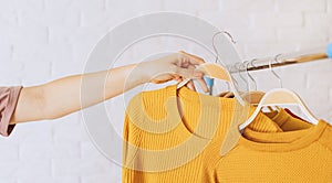Woman& x27;s hand removes yellow knitted jacket on wooden hanger from an iron rack rale photo