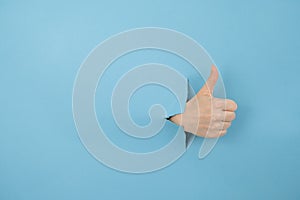 A woman's hand sticking out of a hole from a blue background shows a thumbs up.