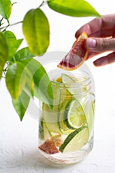 A woman's hand throws a slice of red orange into a glass mug with handle with refreshing detox lemonade with sliced