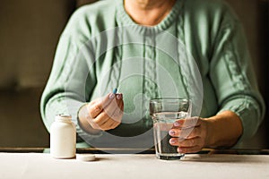 Woman& x27;s hands holds a blue capsule and glass of water over the table, ready to take medicines. Health care concept.