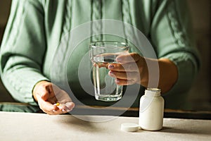 Woman& x27;s hands holds two capsules and glass of water over the table, ready to take medicines. Health care concept.