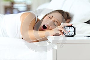 Woman yawning at wakeup turning off alarm clock photo