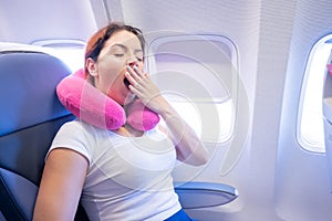 Woman yawns while sitting on the plane by the window.