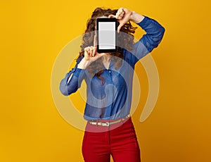 Woman on yellow background hiding behind tablet PC blank screen