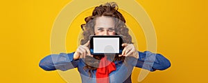 Woman on yellow background hiding behind tablet PC blank screen