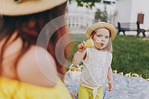 Woman in yellow clothes play on grass in park rest, amuse with little cute child baby girl blowing soap bubbles. Mother