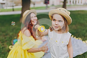 Woman in yellow clothes play on grass in park rest, amuse with little cute child baby girl blowing soap bubbles. Mother