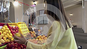 Woman in yellow coat chooses a fresh fruits at market