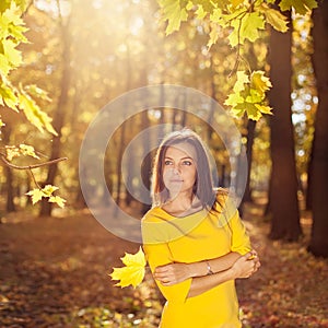 Woman in the yellow dress with autumn leaves in hand and fall yellow maple garden background