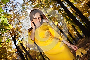 Woman in the yellow dress with autumn leaves in hand and fall yellow maple garden background