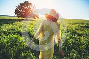 Woman in yellow dress and hat walking in summer field in sunlght