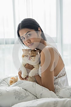 woman and yellow exotic shorthair cat on bed