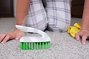 Woman in yellow gloves with a green brush cleaning and brushing carpet, removing stains and wool from it and doing routine