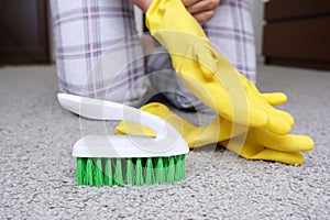 Woman in yellow gloves with a green brush cleaning and brushing carpet, removing stains and wool from it and doing routine