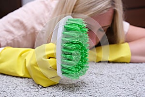 Woman in yellow gloves with a green brush is so tired of cleaning and brushing carpet, removing stains and wool from it