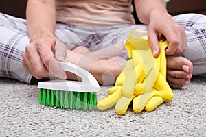 Woman in yellow gloves with a green brush is so tired of cleaning and brushing carpet, removing stains and wool from it and doing