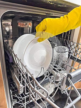 woman in yellow gloves loading dishes in dishwasher machine. Kitchen appliances, lifestyle