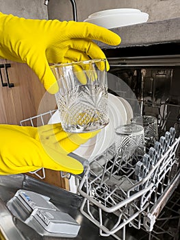 woman in yellow gloves loading dishes in dishwasher machine. Kitchen appliances, lifestyle