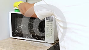 Woman in yellow gloves scrub outer surface of microwave with brush with detergent in kitchen. Housewife carry out wet