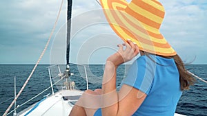 Woman in a yellow hat and blue dress girl rests aboard a yacht near the lighthouse on summer season at ocean. Slow