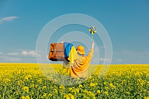 Woman in yellow hoodie with pinwheel and suitcase in rapeseed field