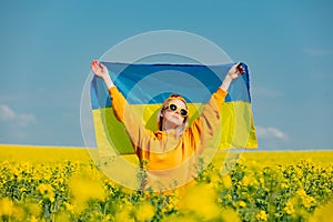 Woman in yellow hoodie and ukrainian flag in rapeseed field