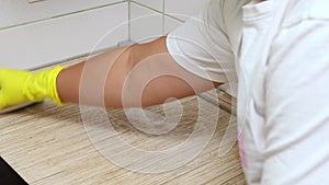 Woman in yellow household gloves spray cleanser on surface of kitchen panel then rub with brush. Housewife carry out wet