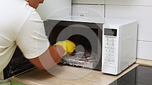 Woman in yellow household gloves wipe inside of microwave with cleaning rag in kitchen. Housewife carry out wet cleaning