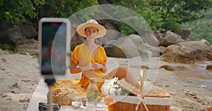 Woman in a yellow outfit filming for her vblog, streaming online from the beach for her followers