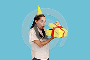 Woman in yellow party cone looking into gift box, opening present and peeking inside with shock.