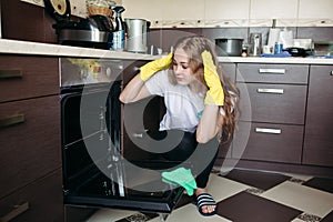 Woman in yellow protective gloves looking dirty oven at home kitchen.