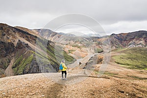 Woman in yellow raincoat hiking in the colourful mountains in Landmannalaugar national park, Iceland