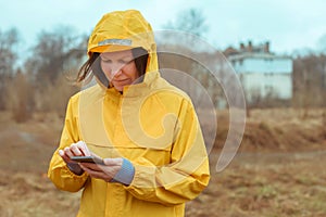 Woman in yellow raincoat texting on mobile phone outdoors