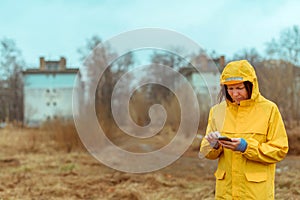 Woman in yellow raincoat texting on mobile phone outdoors