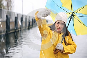 Woman in yellow raincoat with umbrella caught in gust of wind near river