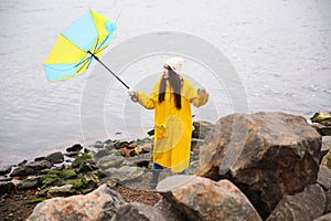 Woman in yellow raincoat with umbrella caught in gust of wind near river