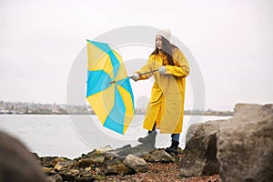 Woman in yellow raincoat with umbrella caught in gust of wind near river