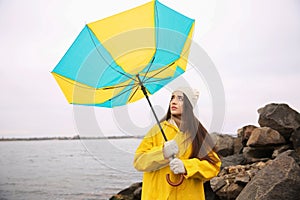 Woman in yellow raincoat with umbrella caught in gust of wind near river