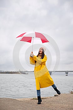 Woman in yellow raincoat with umbrella caught in gust of wind near river