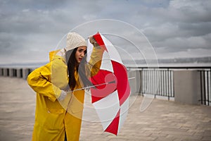 Woman in yellow raincoat with umbrella caught in gust of wind outdoors