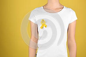 Woman with yellow ribbon on color background. Cancer awareness concept