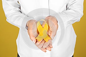 Woman with yellow ribbon on color background, closeup. Cancer awareness concept