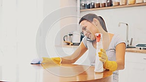 Woman in yellow rubber gloves is cleaning cooking panel in kitchen with fat remover spray and a cloth. Crop. Copy space