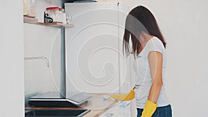 Woman in yellow rubber gloves is cleaning cooking panel in kitchen with fat remover spray and a duster. Close up. 4K.