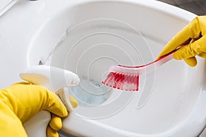Woman in yellow rubber gloves cleaning toilet bowl with red brush