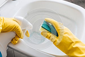 Woman in yellow rubber gloves cleaning toilet with detergent