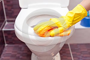 Woman in yellow rubber gloves cleaning toilet seat with orange cloth. Bathroom and toilet hygiene.