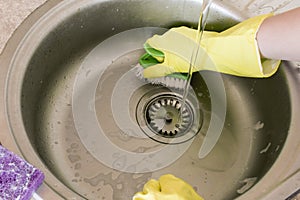 Woman in yellow rubber gloves washes and cleans a sink with a sponge and brush.