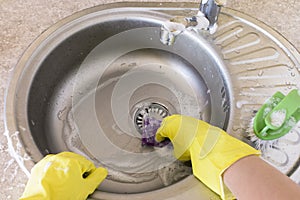 Woman in yellow rubber gloves washes and cleans a sink with a sponge and brush.